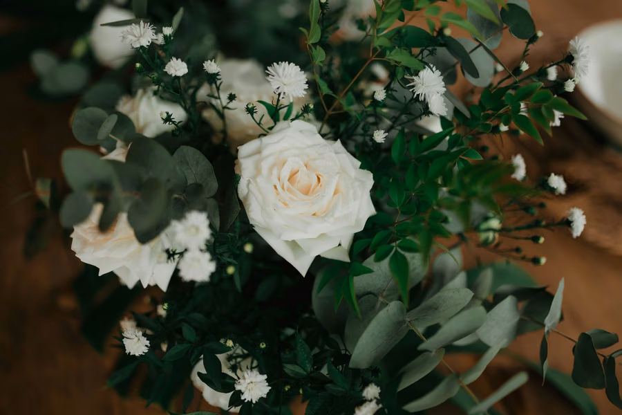 Arranjo de rosas brancas com folhagens sobre mesa de madeira